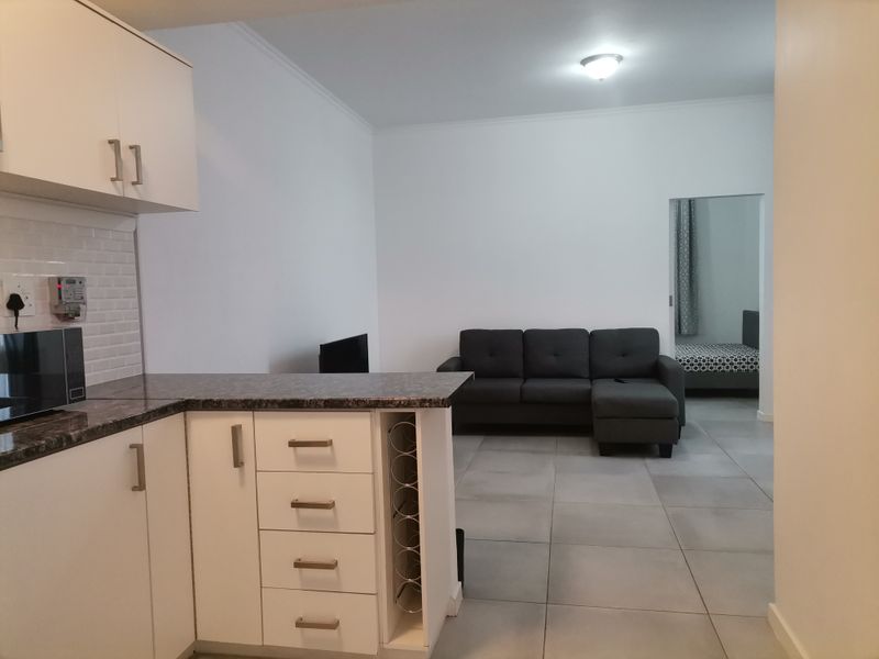 An open-plan living area featuring a modern kitchen with white cabinetry, subway tile backsplash, and tiled flooring, flowing into a comfortable lounge space.
