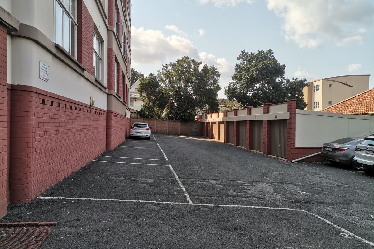 Exterior view of the apartment building rear parking area featuring a row of garages and marked parking bays.