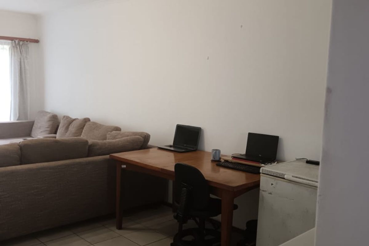 A functional living area featuring neutral ceramic floor tiles and coved ceilings, providing a versatile space for relaxation or a home office setup.