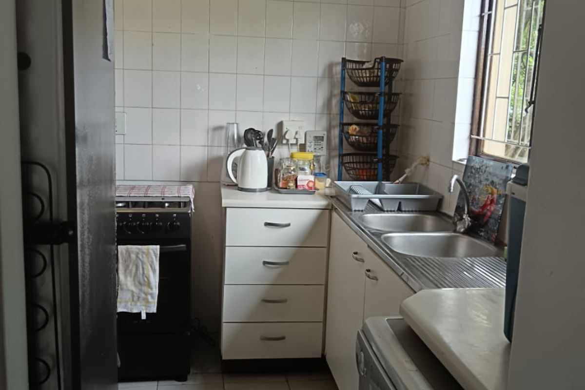 A compact kitchen featuring tiled splashbacks, built-in cabinetry, a double stainless steel sink, and a freestanding stove.