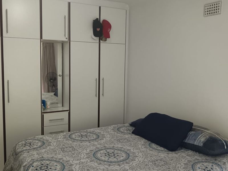 A bedroom featuring white built-in wardrobes with integrated shelving and a central mirror, providing ample storage space.