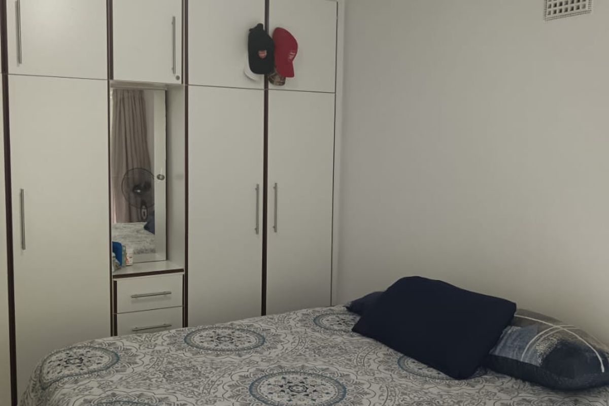 A bedroom featuring white built-in wardrobes with integrated shelving and a central mirror, providing ample storage space.