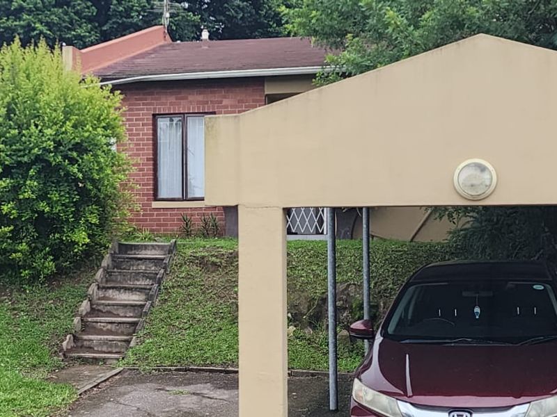 Front view of the townhouse featuring a covered carport, brick exterior facade, and concrete steps leading to the entrance.