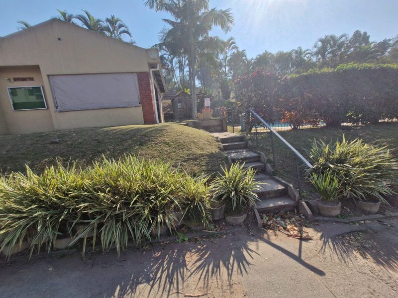 Rear exterior view of the townhouse featuring concrete stairs with a metal handrail leading to a landscaped garden area.