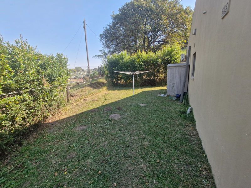 A rear garden area featuring a lawn, established hedging, and an exterior wall with a utility shed.
