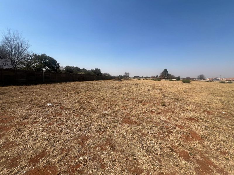A wide, vacant residential plot featuring dry grass and a timber boundary fence, offering a blank canvas for future development.