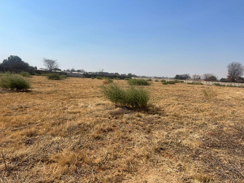 A wide-angle view of a vacant residential plot featuring dry grass and perimeter fencing, offering a blank canvas for future development.
