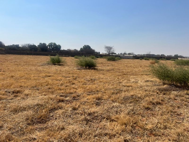 A wide-angle view of a vacant residential plot featuring dry grass and a perimeter boundary wall.