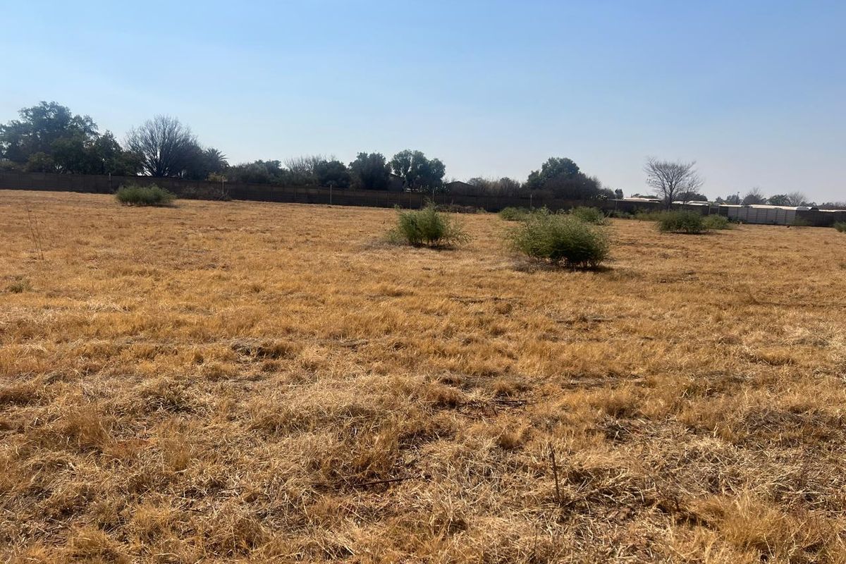 A wide-angle view of a vacant residential plot featuring dry grass and a perimeter boundary wall.