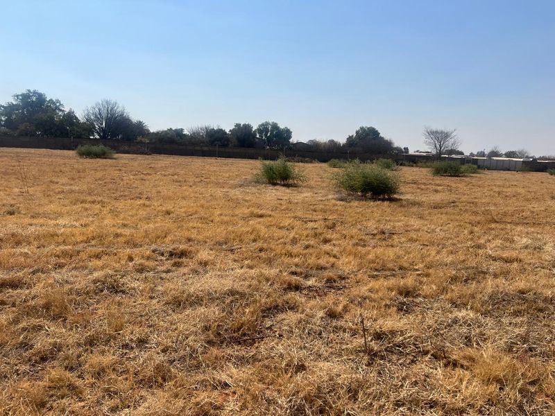 A wide-angle view of a vacant residential plot featuring dry grass and a perimeter boundary wall.