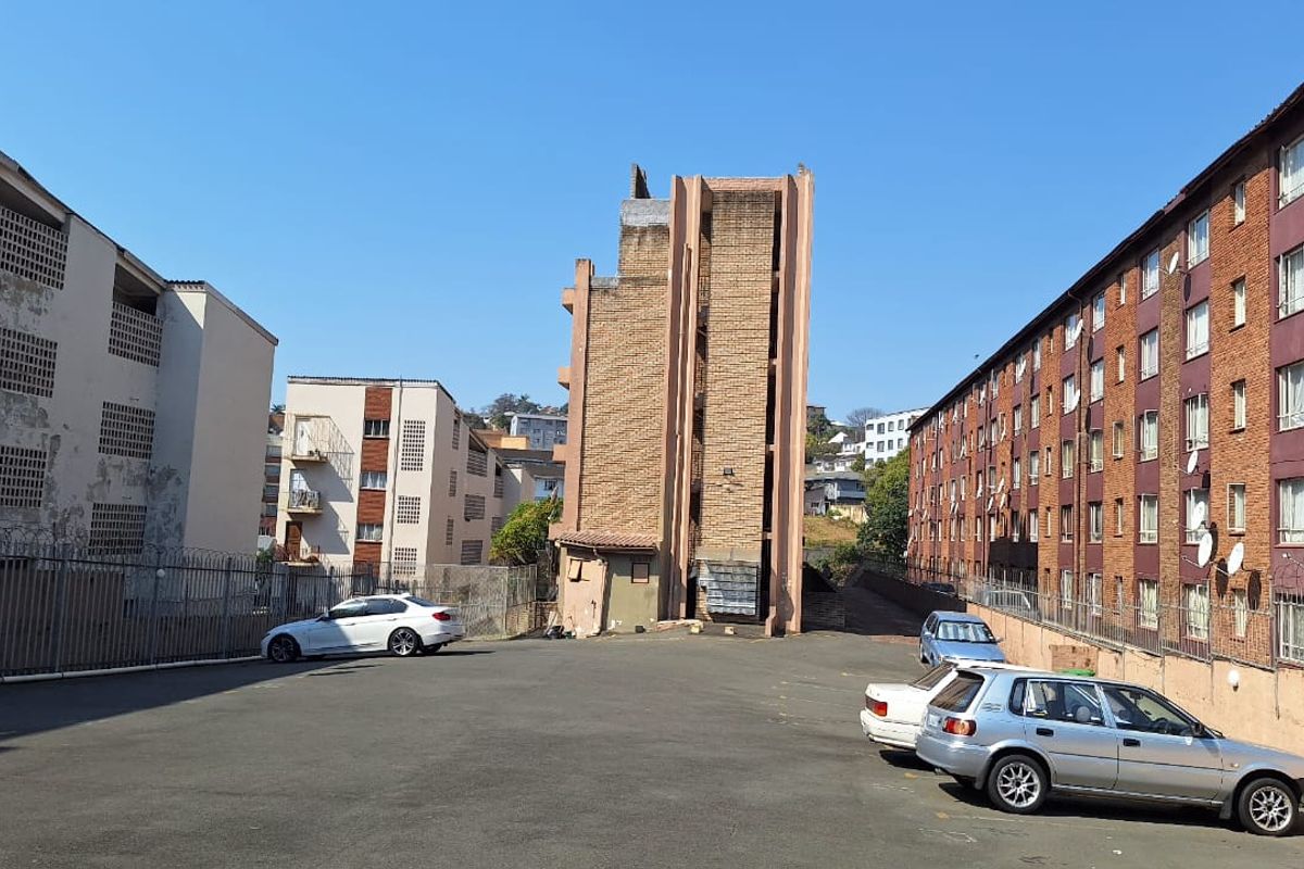 Exterior view of the apartment complex showing the rear parking area, brick building facades, and security fencing.