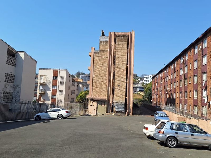 Exterior view of the apartment complex showing the rear parking area, brick building facades, and security fencing.