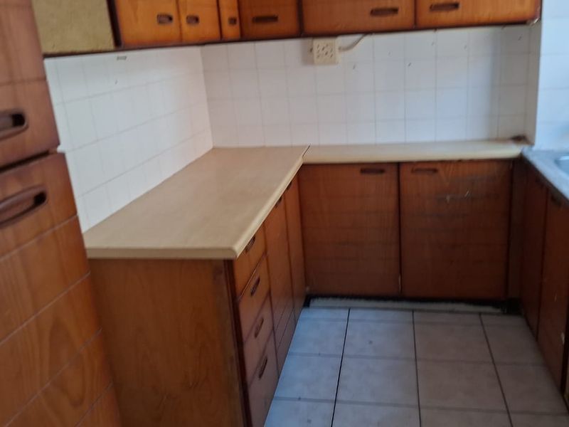 A dated kitchen featuring original wooden cabinetry, laminate countertops, and a stainless steel sink, offering significant potential for a modern renovation.