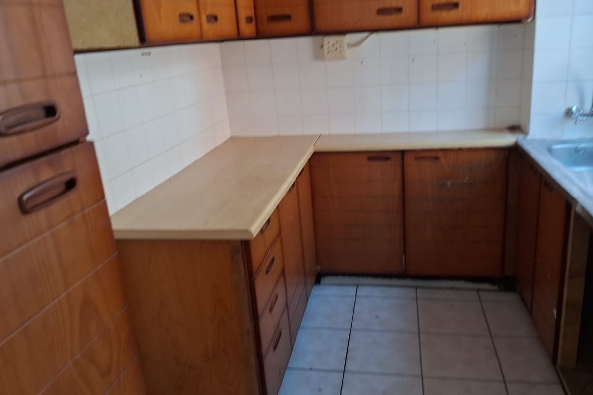 A dated kitchen featuring original wooden cabinetry, laminate countertops, and a stainless steel sink, offering significant potential for a modern renovation.