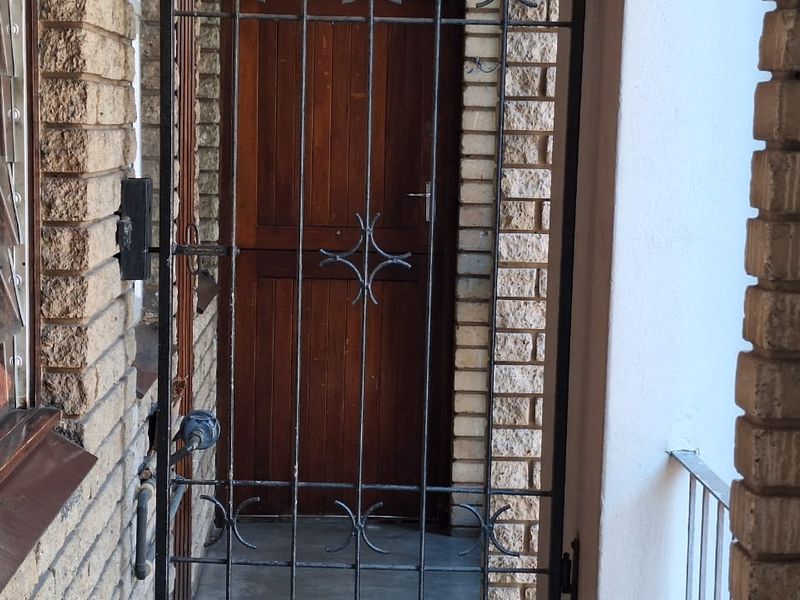 Entrance area featuring a timber door protected by a metal security gate, set within a face brick facade.