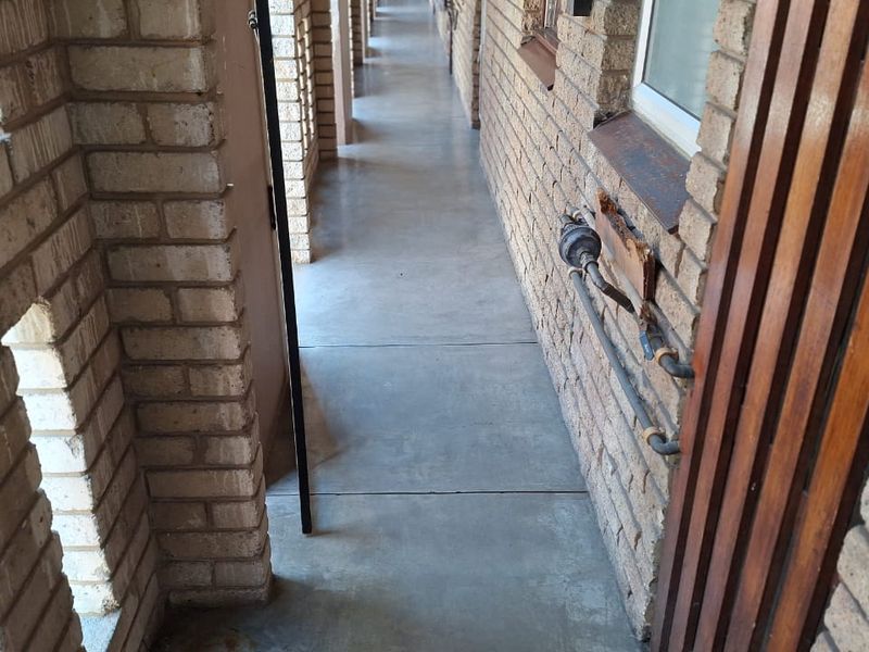 An exterior apartment building walkway featuring exposed brick walls, concrete flooring, and visible utility piping.