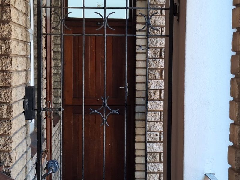 Entrance area featuring a secure metal gate, solid timber door, and textured brick facade with louvre window detailing.