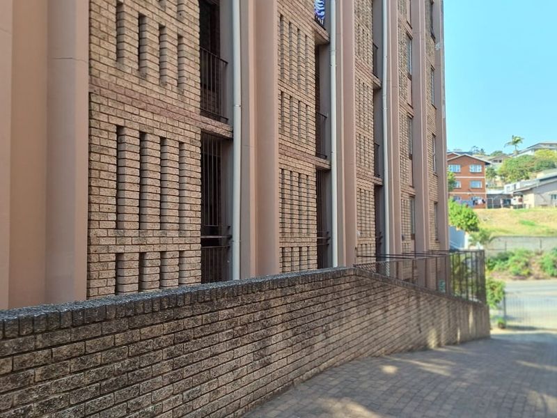 Exterior view of the apartment building facade featuring brick construction, a paved driveway, and a retaining wall.