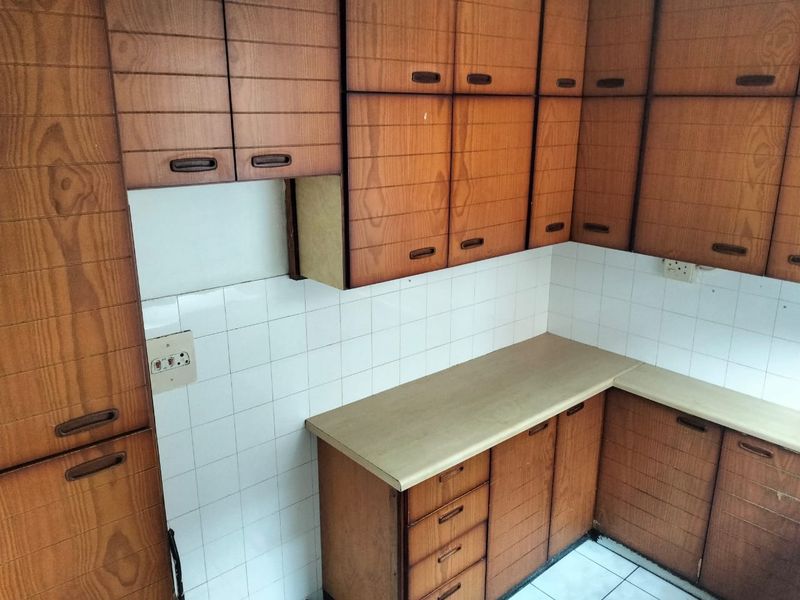 A dated kitchen featuring original wood-look laminate cabinetry, tiled splashbacks, and ample counter space, offering significant potential for a modern renovation.