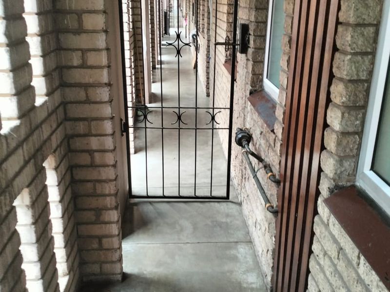 An exterior apartment building walkway featuring exposed brick walls, concrete flooring, and a metal security gate.