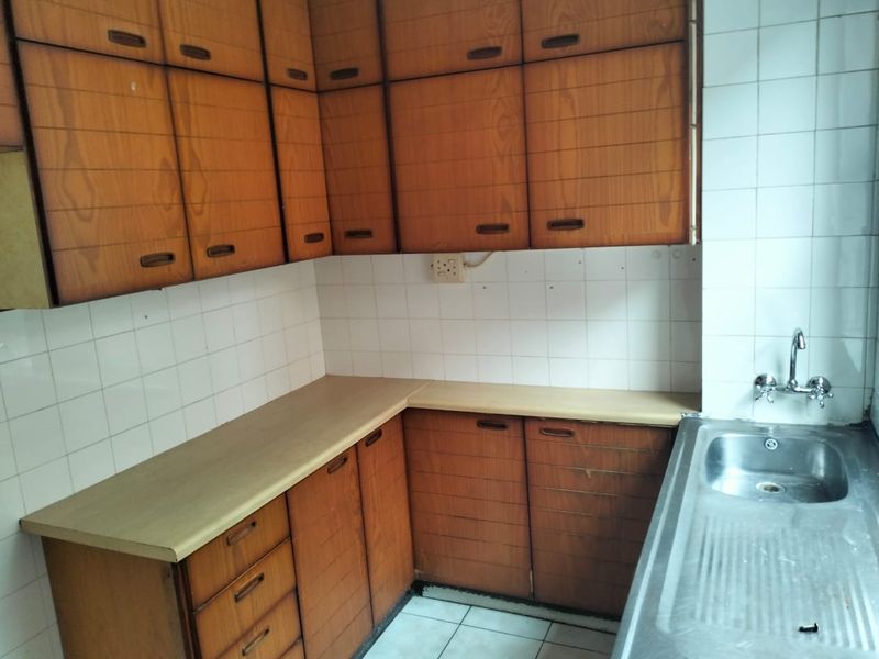 A dated kitchen featuring original wood-look laminate cabinetry, a stainless steel sink, and tiled backsplash, offering significant potential for a modern renovation.