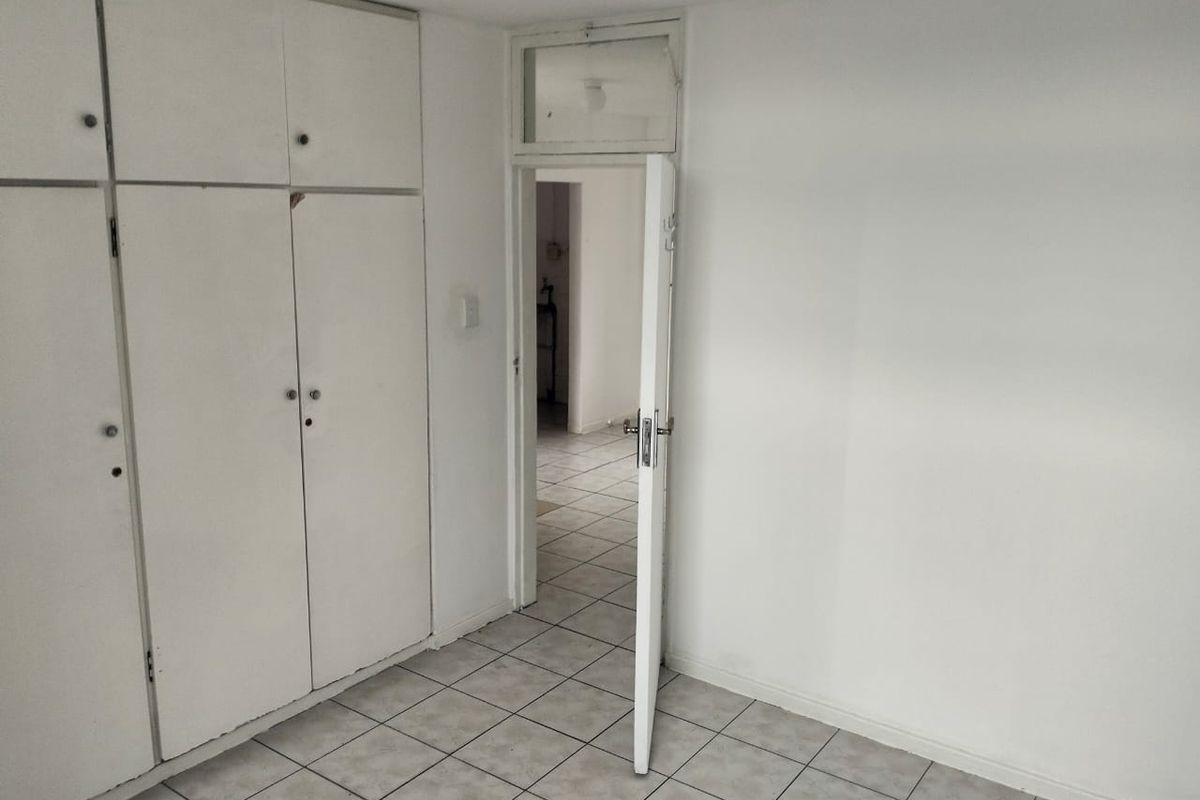 An empty bedroom featuring tiled flooring and built-in cupboards, offering a blank canvas for potential interior design updates.