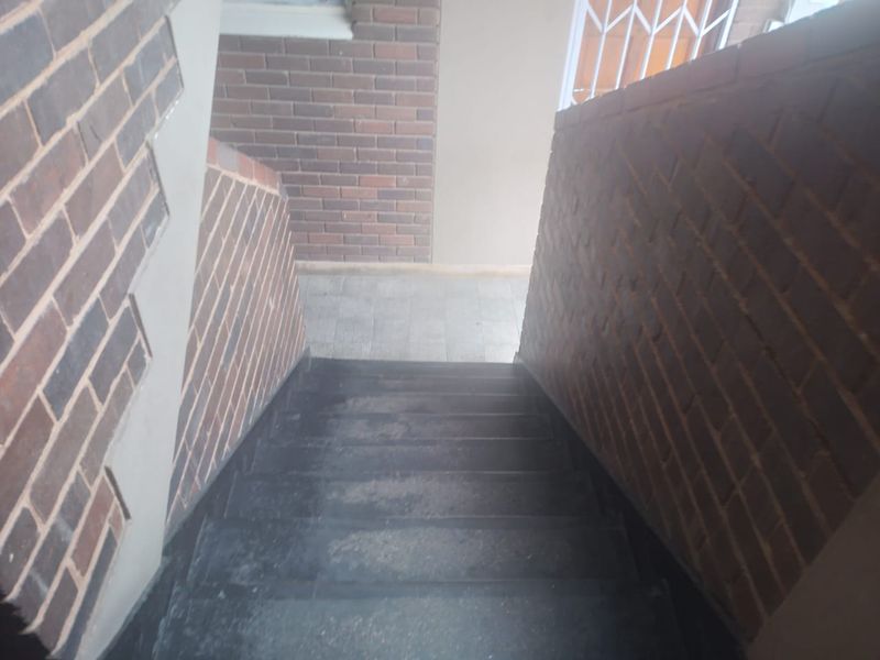 A view looking down a staircase featuring brick walls and a security gate, showing signs of wear on the stair treads.