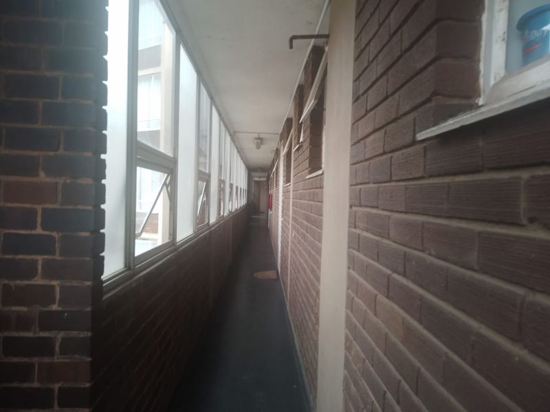 A long, narrow apartment hallway featuring exposed brick walls and large glass window panels along one side.