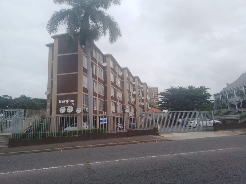 Street view of the Berglen apartment complex, featuring a multi-story brick building with secure perimeter fencing and gated access.