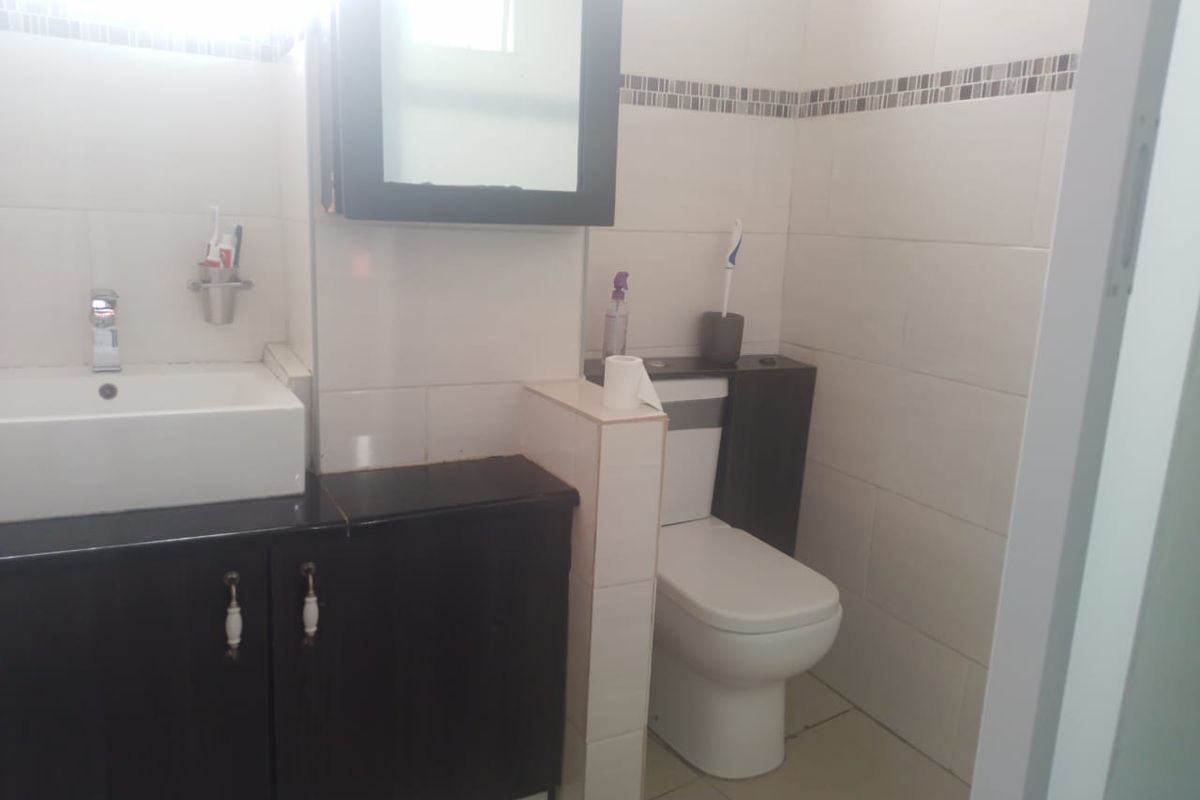 A functional bathroom featuring a vanity cabinet with basin, wall-mounted medicine cabinet, and a standard toilet with tiled wall and floor finishes.