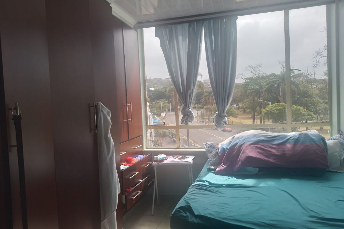 A bedroom featuring built-in cupboards, tiled flooring, and a large window offering an exterior view.