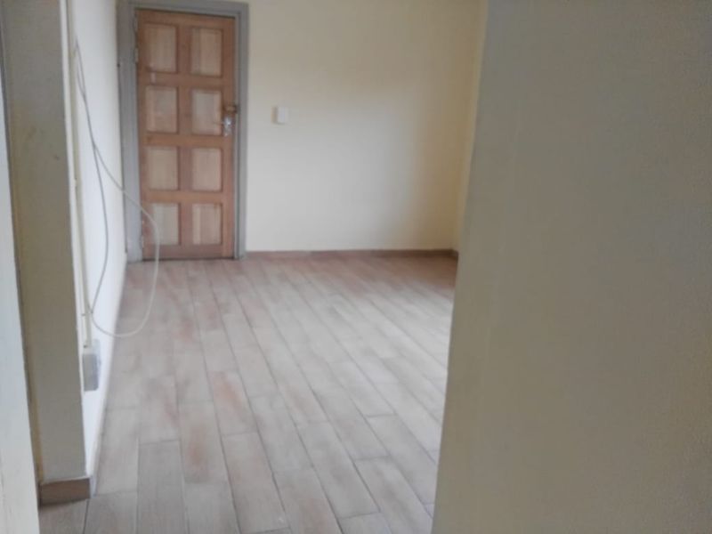 An empty bedroom featuring tiled flooring and a wooden door, requiring minor cosmetic updates to improve its overall appeal.