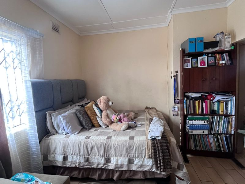 A bedroom featuring tiled flooring, a window with a security gate, and standard ceiling cornicing. The walls show signs of wear and require repainting.