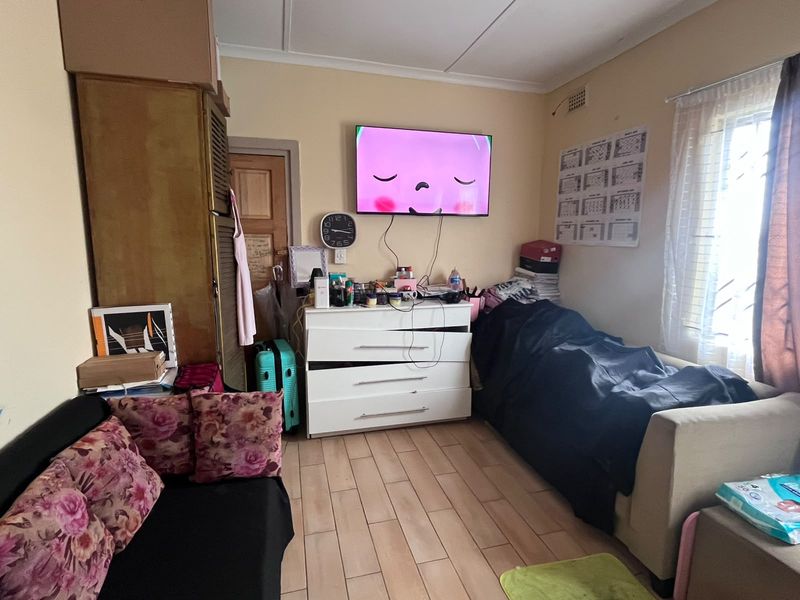 A bedroom featuring tiled flooring, a built-in cupboard, and a window with security bars. The room requires cosmetic updates and repairs.