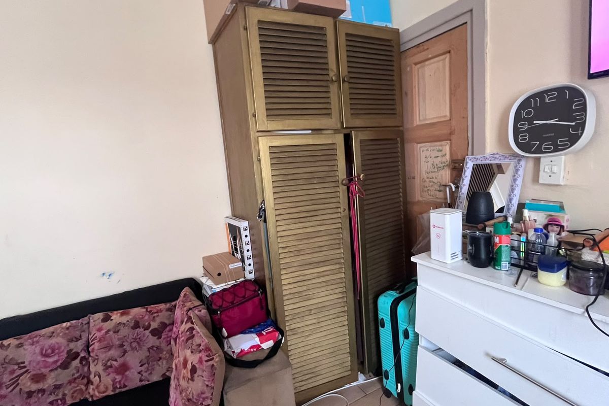 A bedroom interior featuring a built-in cupboard with louvered doors, showing signs of wear on the surrounding wall and door frame.