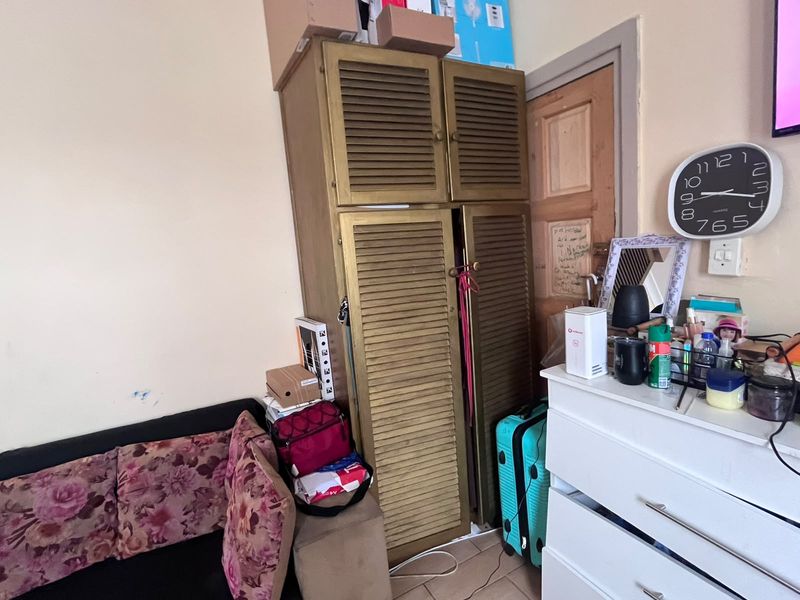 A bedroom interior featuring a built-in cupboard with louvered doors, showing signs of wear on the surrounding wall and door frame.