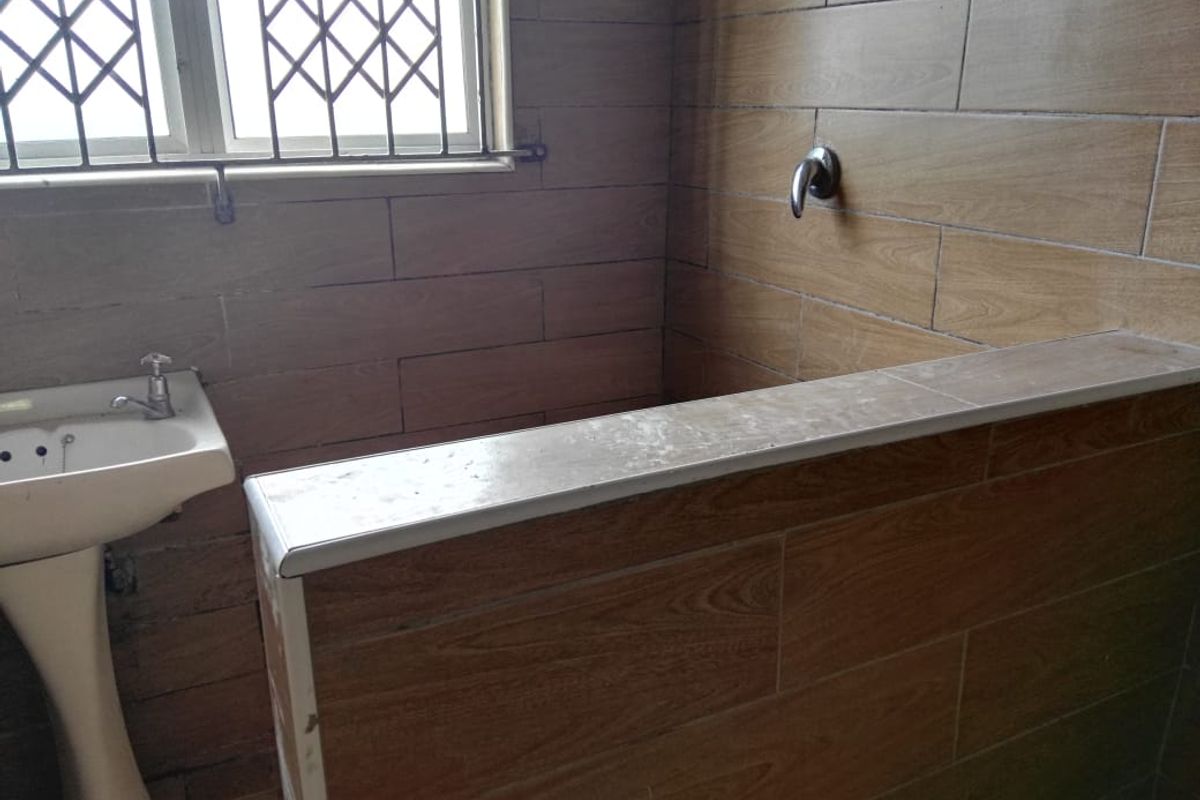 A dated bathroom featuring wood-look wall tiles, a pedestal basin, and a shower area with a built-in tiled ledge.