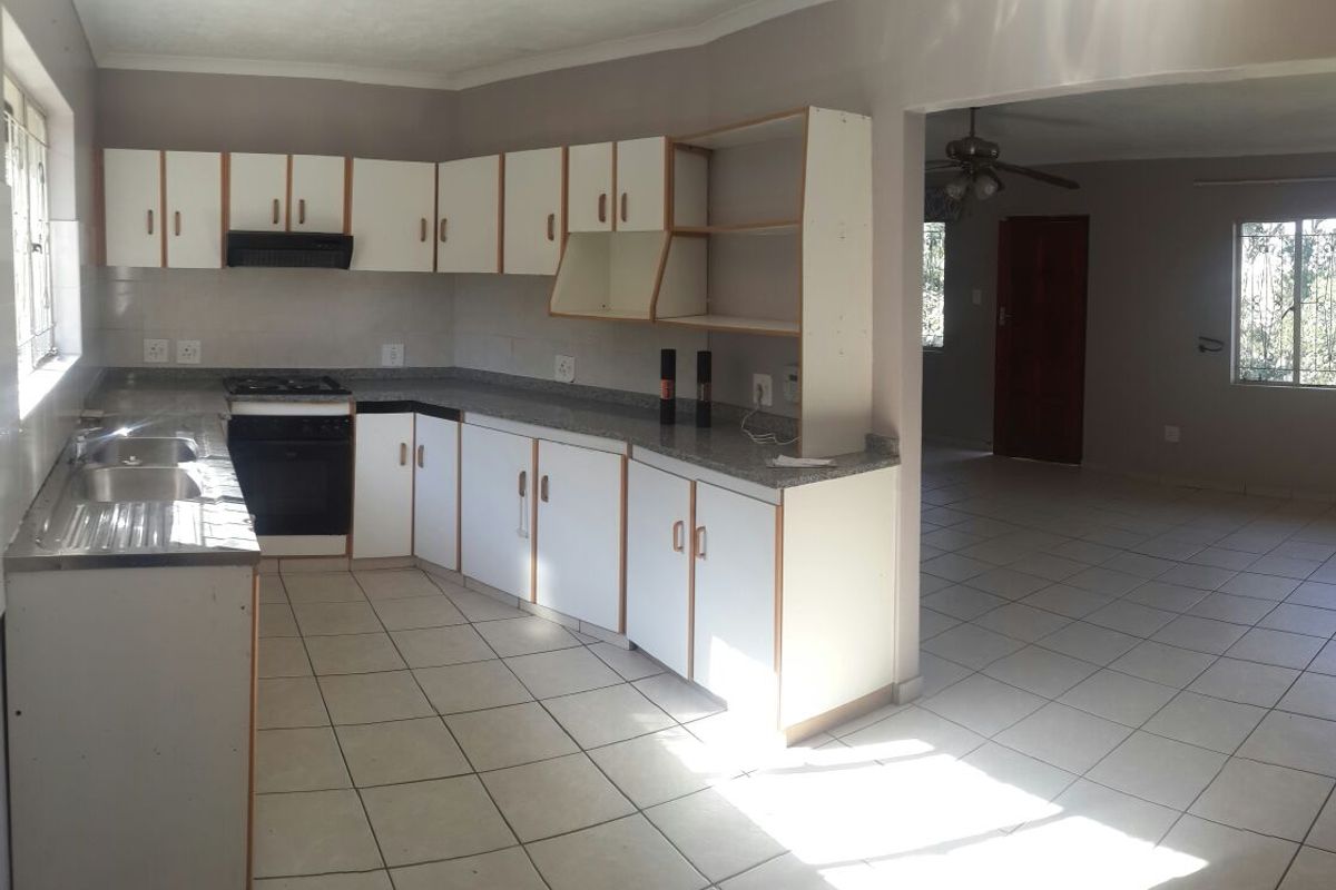A functional, empty kitchen featuring white cabinetry, laminate countertops, a built-in oven with gas hob, and tiled flooring, opening into an adjacent living area.