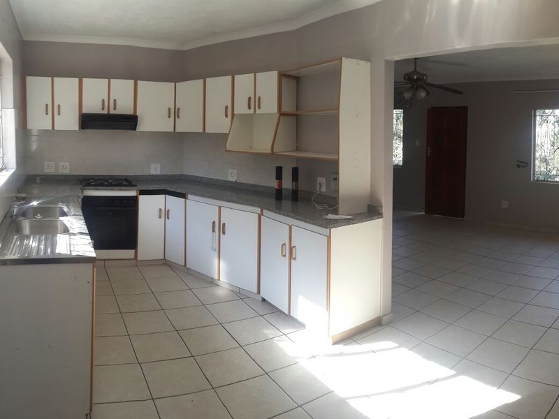 A functional, empty kitchen featuring white cabinetry, laminate countertops, a built-in oven with gas hob, and tiled flooring, opening into an adjacent living area.