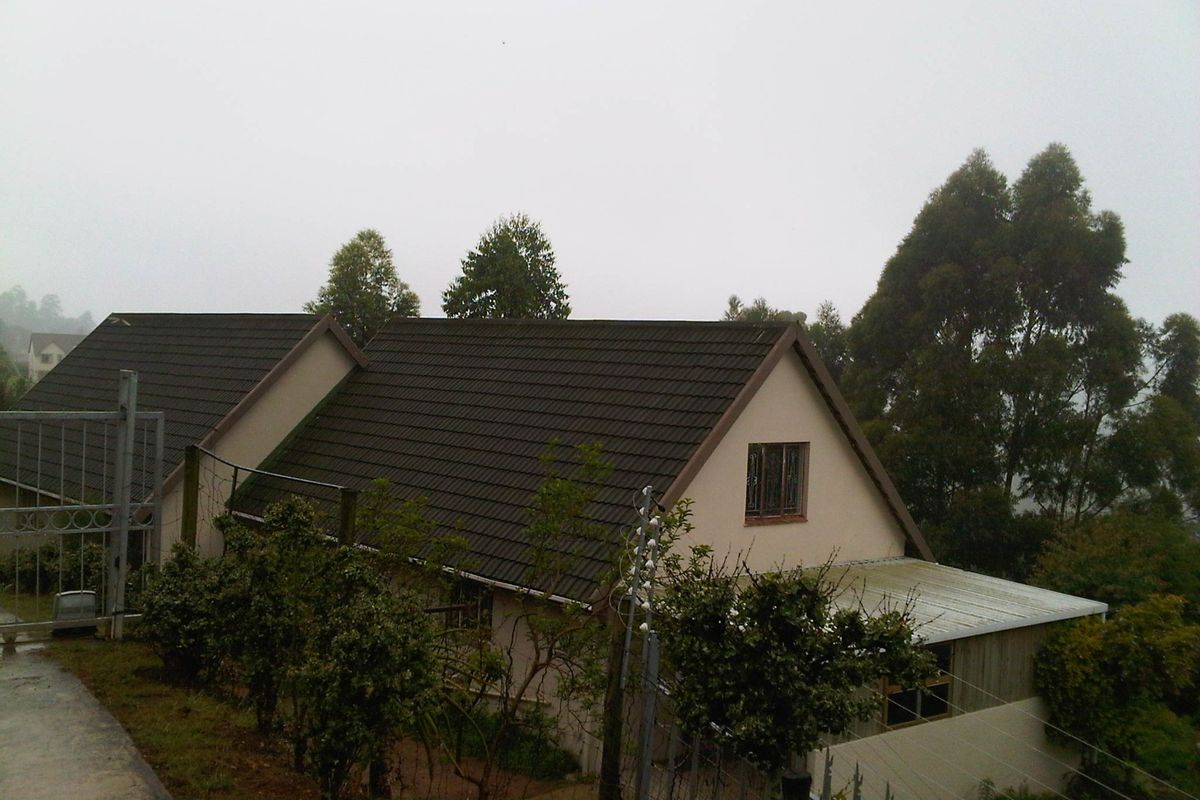 Rear view of the townhouse featuring a tiled roof, concrete driveway, and perimeter electric fencing in a quiet, misty setting.