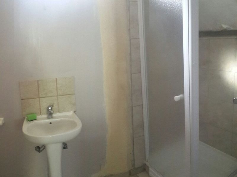 A functional bathroom featuring a pedestal basin and a shower enclosure, currently requiring cosmetic updates to the wall finishes.