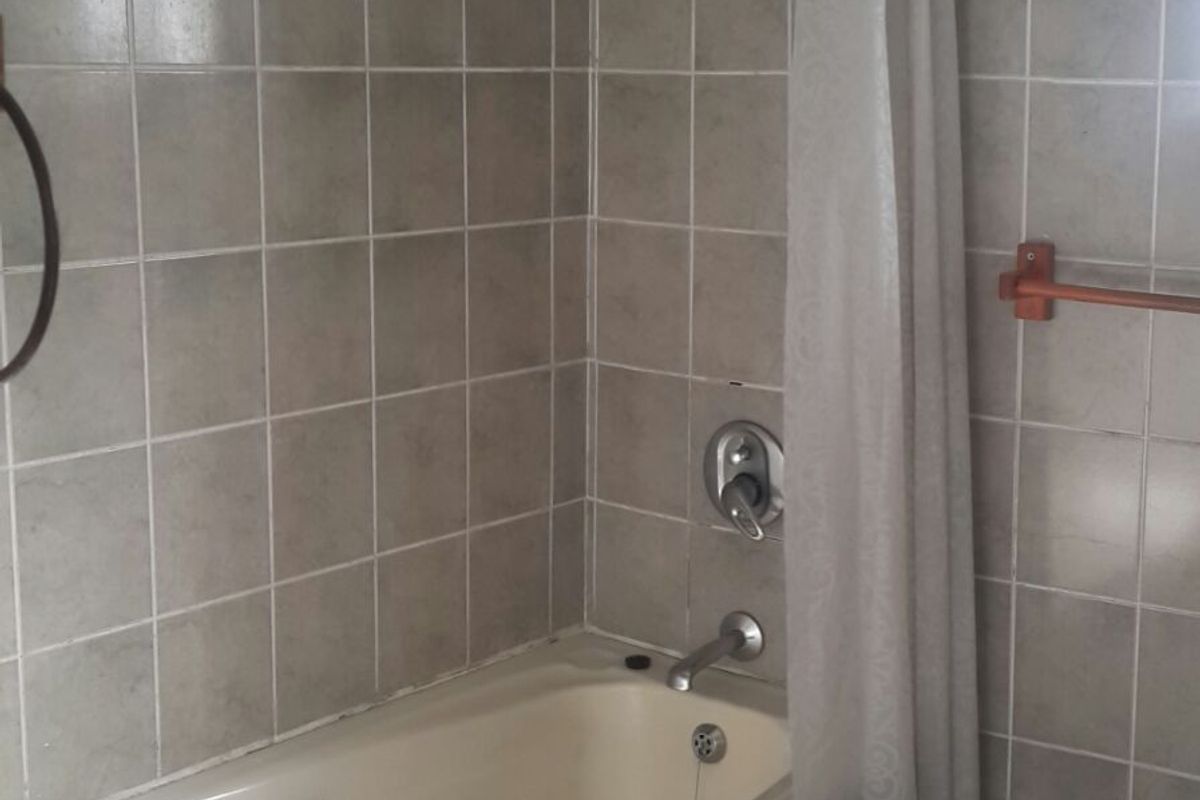 A dated bathroom featuring a built-in bathtub with shower attachment, tiled walls, and floor, requiring cosmetic updates to modernize the space.