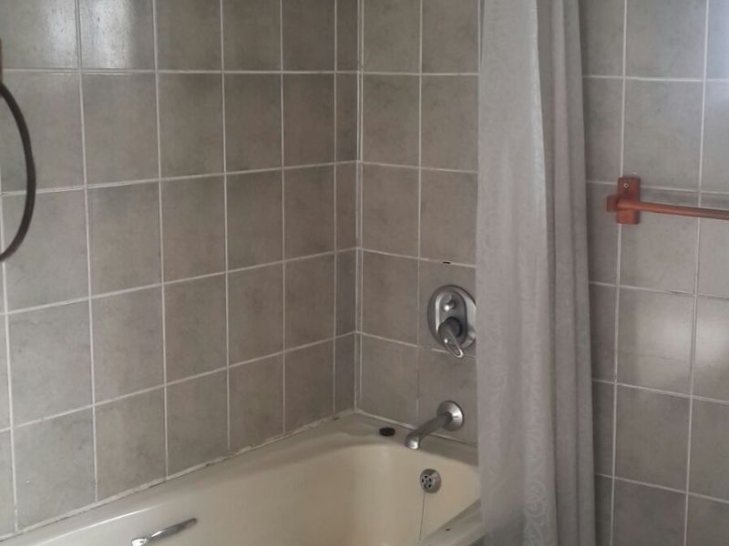 A dated bathroom featuring a built-in bathtub with shower attachment, tiled walls, and floor, requiring cosmetic updates to modernize the space.