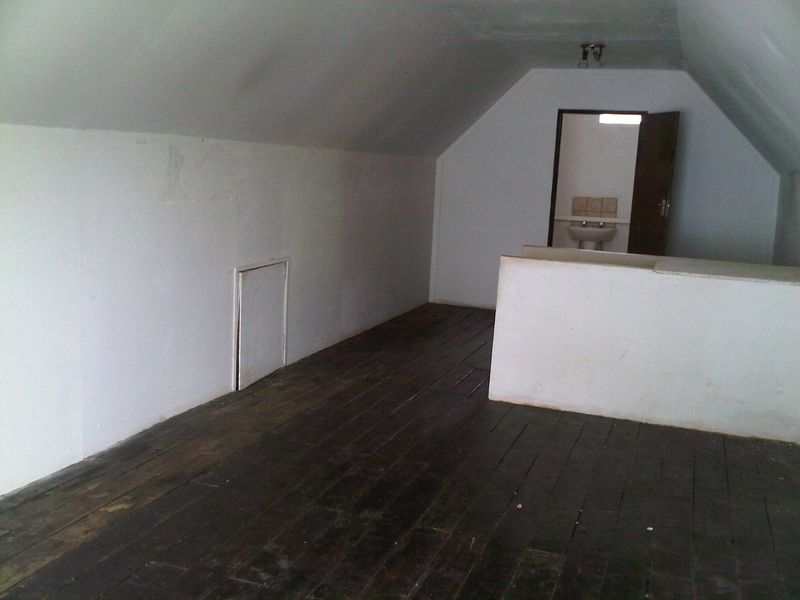 An empty attic-style bedroom featuring sloped ceilings, dark timber flooring, and direct access to an en-suite bathroom.
