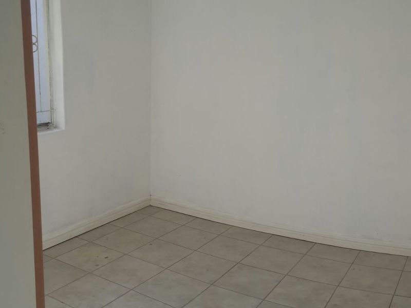 An empty bedroom featuring tiled flooring and a window with security bars, presenting a blank canvas for potential interior design updates.