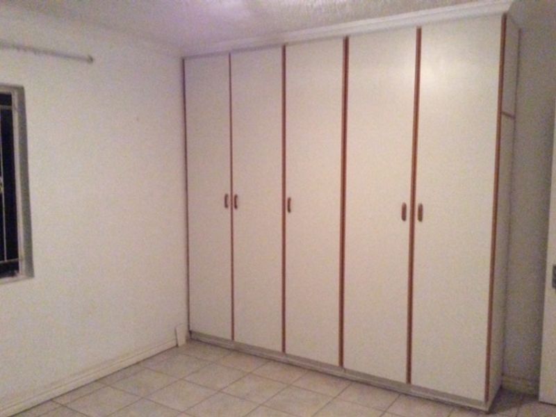 A vacant bedroom featuring built-in cupboards, tiled flooring, and security bars on the window, offering a blank canvas for potential updates.