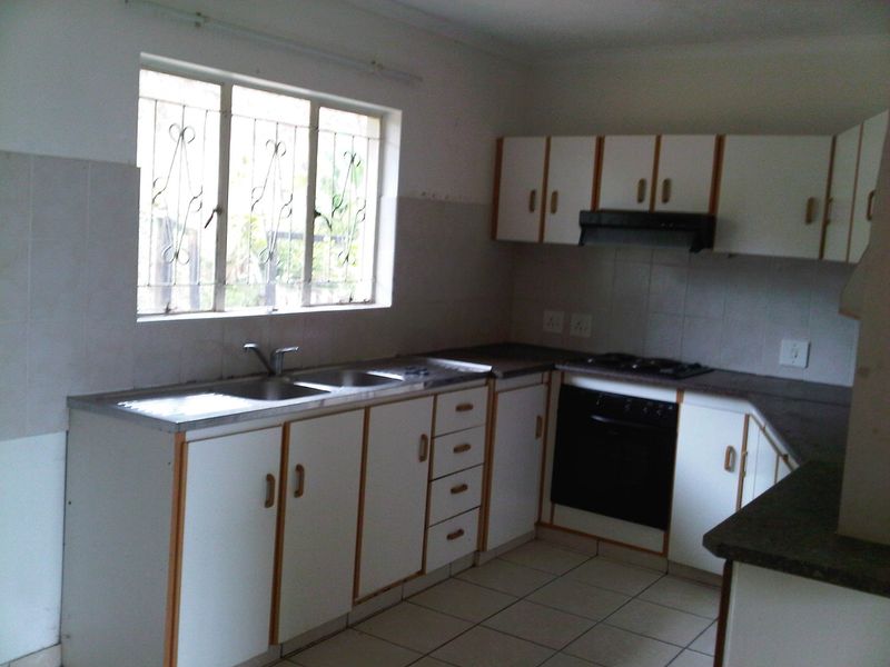 A functional kitchen featuring built-in cabinetry, a double sink, integrated oven, and gas hob, with tiled flooring and security bars on the window.