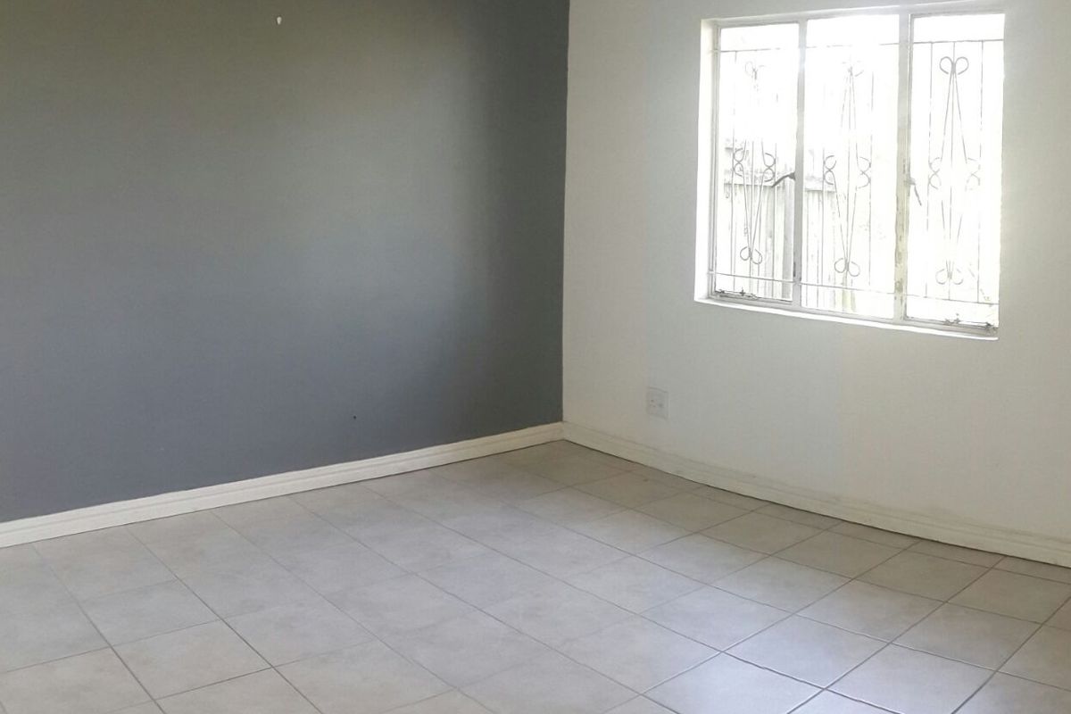 An empty bedroom featuring neutral tiled flooring, a grey accent wall, and a window fitted with security bars.