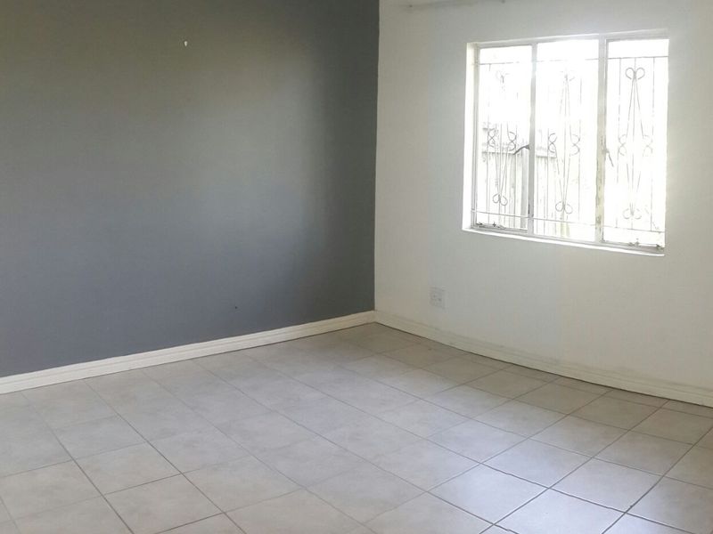 An empty bedroom featuring neutral tiled flooring, a grey accent wall, and a window fitted with security bars.