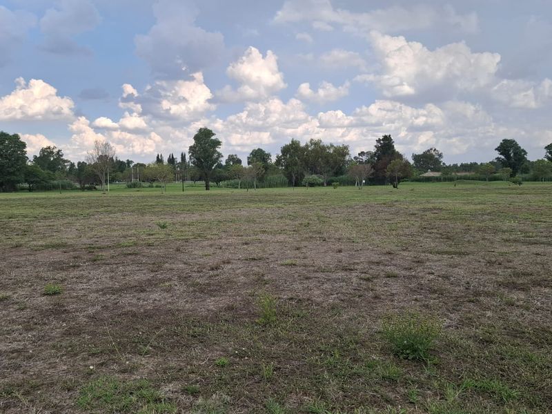 A wide, open expanse of vacant residential land featuring natural grass cover and mature trees in the background.